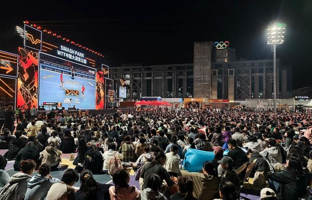 众多乒乓球迷自发聚集在WTT大满贯公园巨幅直播屏幕前，席地而坐共同观看精彩比赛。北京日报客户端记者刘平 摄