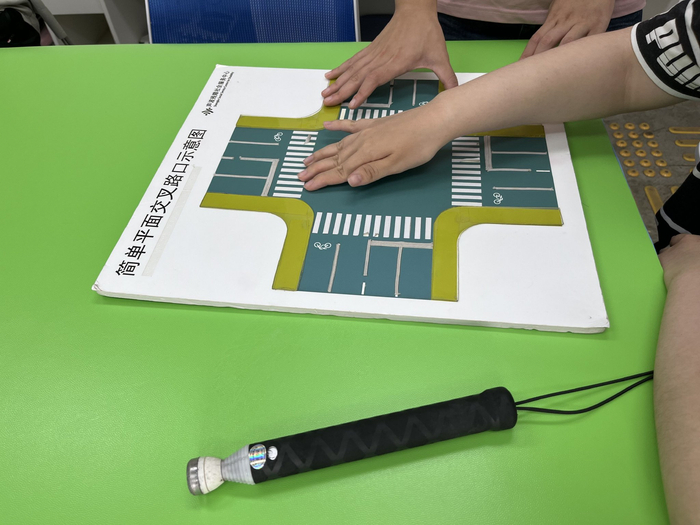 学员们正在用手触摸交叉路口示意图，了解红绿灯、车道和斑马线的方位，一旁是收缩起来的盲杖。新京报记者 徐鸣 摄