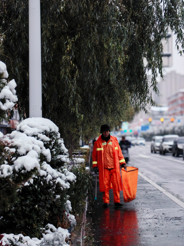 环卫工人已早早开工，橙色的身影在雪中格外醒目。