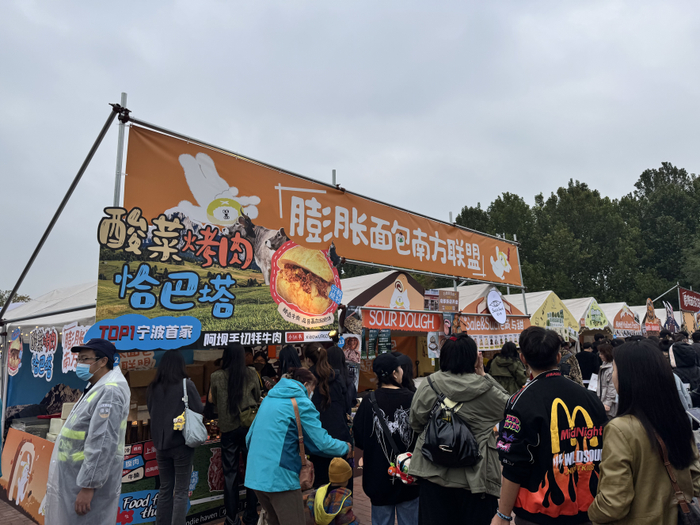 图为酸菜烤肉恰巴塔展位前排起长队的场景。