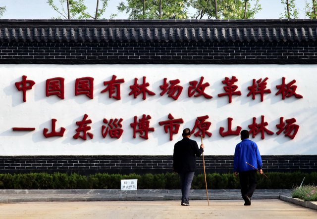 山东淄博原山林场两位晨练的老人从“中国国有林场改革样板”的标语前走过（资料图）。摄影/章轲