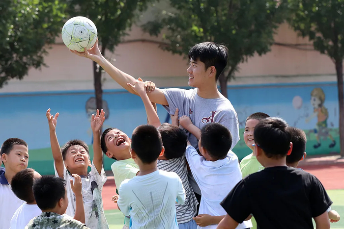 △山东高密，体育老师在操场上与孩子们玩耍。