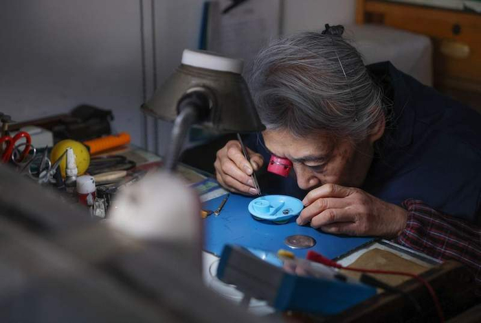 刘宪平戴着寸镜，俯趴在桌前，用镊子挑选细小的零件。