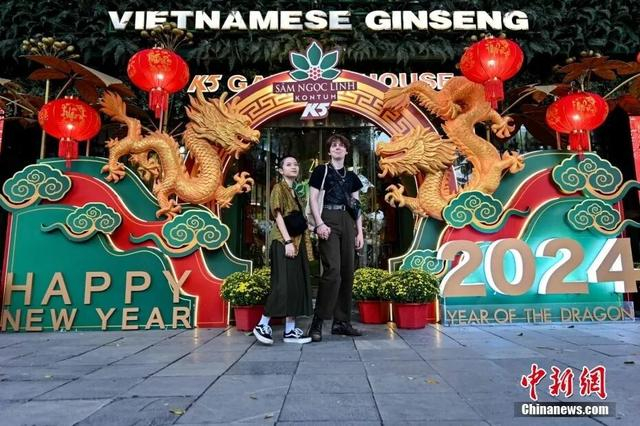 资料图：当地时间2024年2月6日，越南河内，一对夫妇在庆祝中国农历龙年春节的龙形装置前摆姿势拍照。