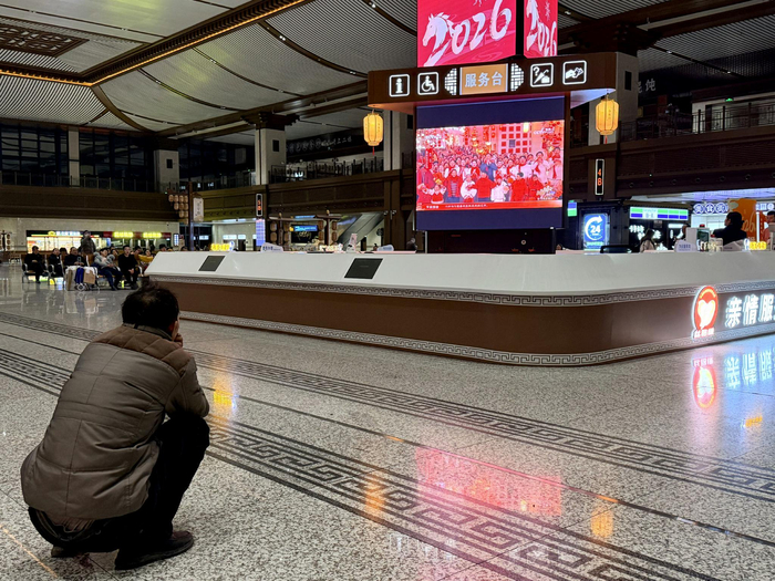 除夕夜，西安火车站候车厅里的屏幕上播放着春晚，一位乘客蹲近观看。新京报记者 丛之翔 摄