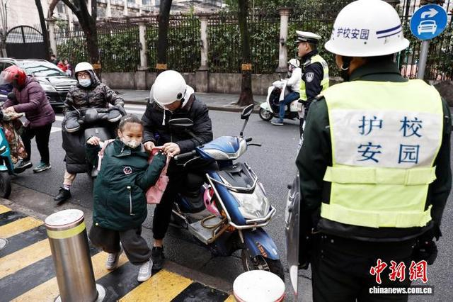 图为在上海市长宁区江苏路第五小学门口，家长帮助学生背书包。中新社记者 殷立勤 摄