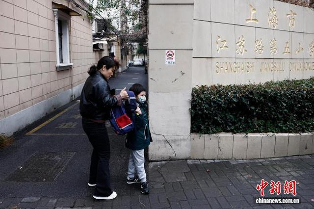 图为在上海市长宁区江苏路第五小学门口，家长帮助学生背书包。中新社记者 殷立勤 摄
