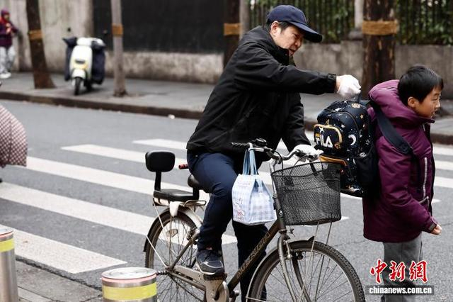 图为在上海市长宁区江苏路第五小学门口，家长帮助学生背书包。中新社记者 殷立勤 摄