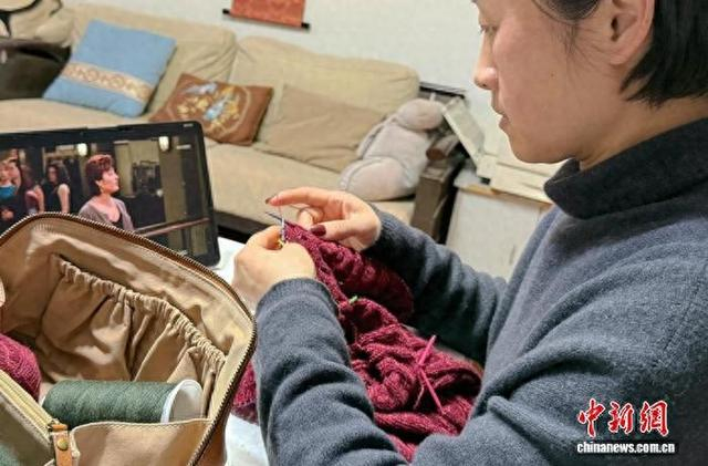 3月6日晚，一名青年在山东烟台家中边追剧边编织。中新社记者 王娇妮 摄