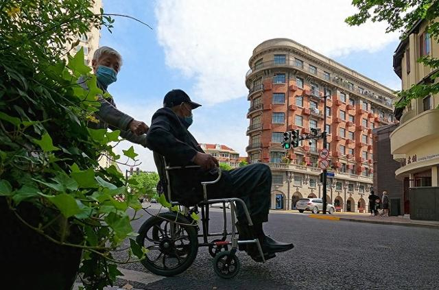 一位老人坐着轮椅路过武康大楼。视觉中国 资料图