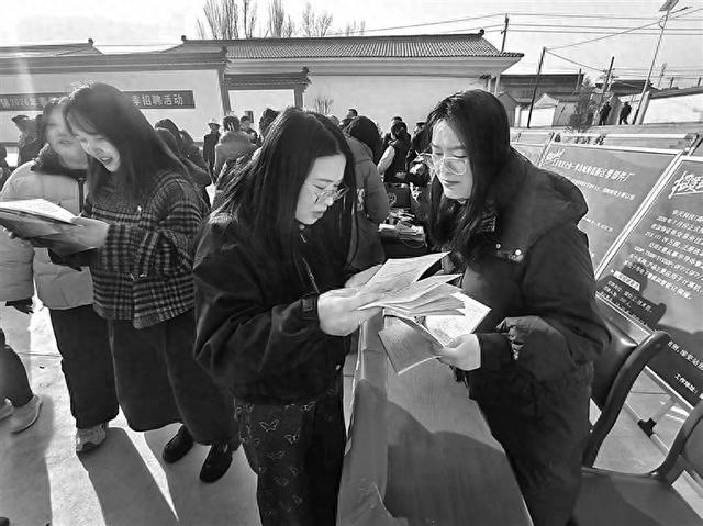 甘肃陇西乡村广场上，务工人员仔细翻阅岗位手册寻找就业机会。邱玥摄/光明图片