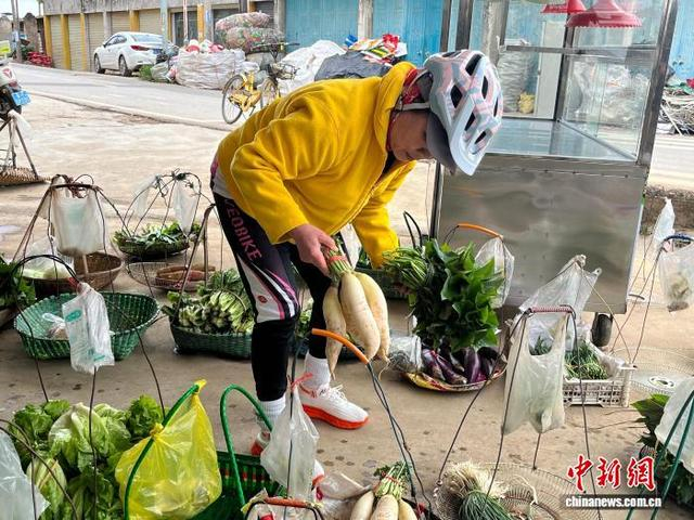 图为骑行爱好者罗丽娟在“无人菜摊”选购蔬菜。韦佳彤 摄