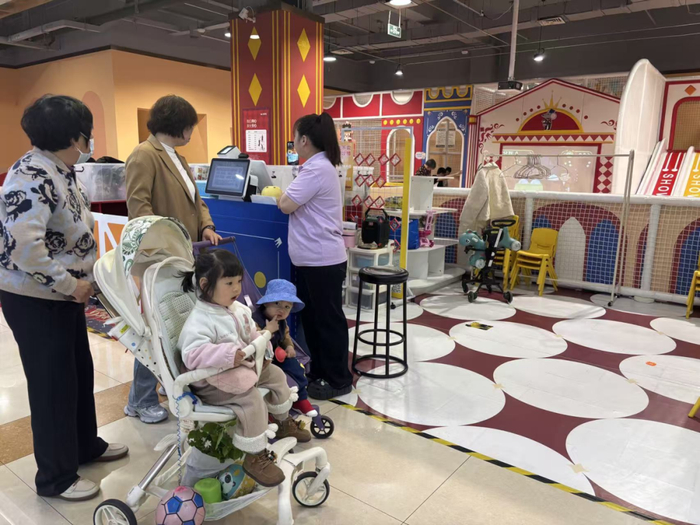 图为家长用推车带孩子来商场体验游乐项目。