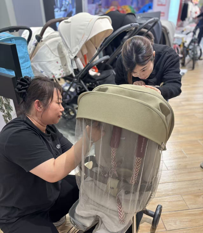 图为销售员在向顾客展示儿童推车的功能。