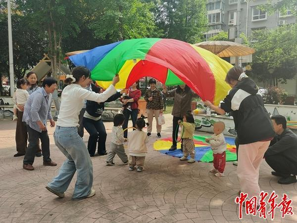 向小会（左）和陈其月（右）在社区用彩虹伞上课，伞下是当天的“学生”。黄晓颖/摄