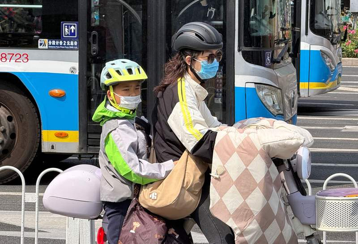 今天上午在崇文门路口，一位家长给乘坐电动车的孩子也戴好了安全头盔。新京报记者 王贵彬 摄