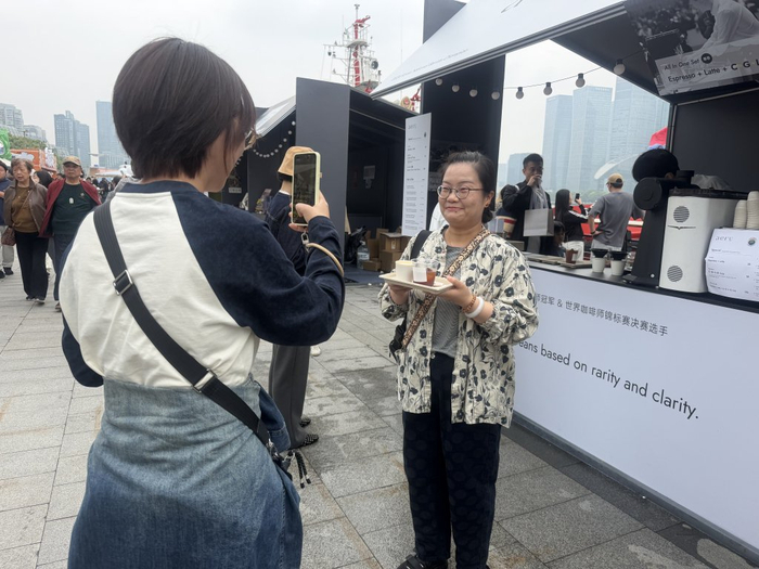 5月3日，2026上海国际咖啡文化节北外滩主会场，游客买到心仪的咖啡，在咖啡摊前打卡。澎湃新闻记者 邹娟 图