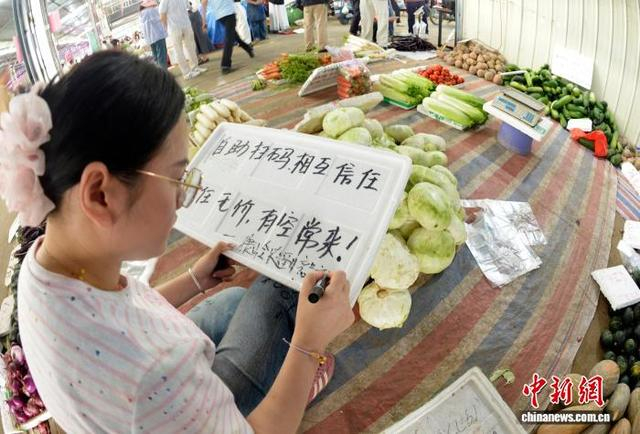 图为“无人值守”蔬菜售卖摊点的摊主在书写广告。滕忠 摄 
