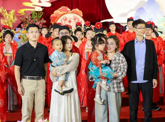 5月20日，山东青岛崂山区，集体婚礼现场，两对往年集体婚礼的参与者，抱着孩子，前来祝贺。张进刚/摄