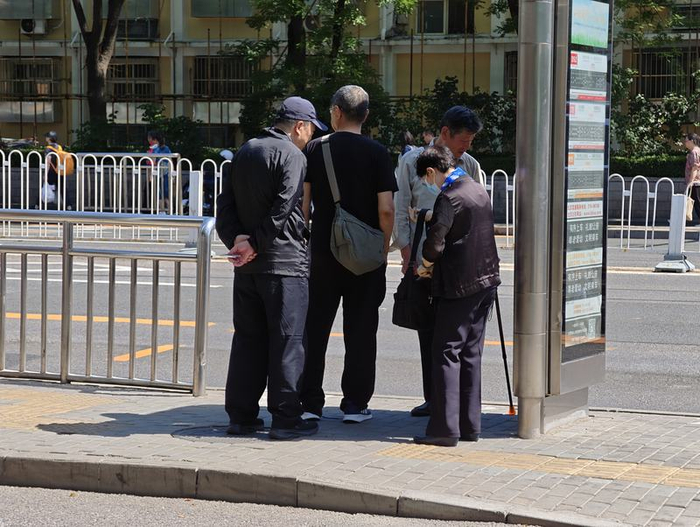 光明楼公交站，乘客纷纷躲在车站牌阴影下候车。