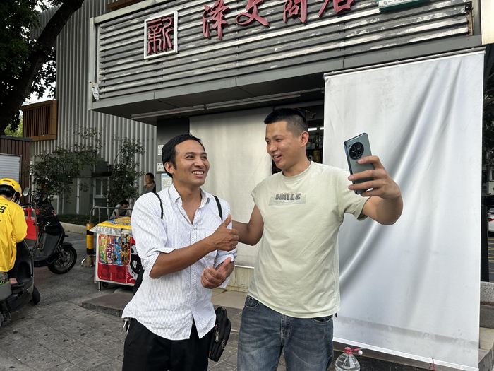 在华强北广场附近的一家店铺门前，有人认出了“卷尺哥”，举起手机和他合影。新京报记者 胡倩 摄