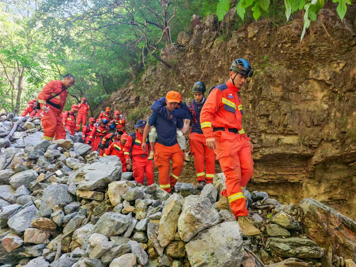 6月4日，京西山区，消防员们背着被困儿童通过碎石路段。房山消防救援支队供图