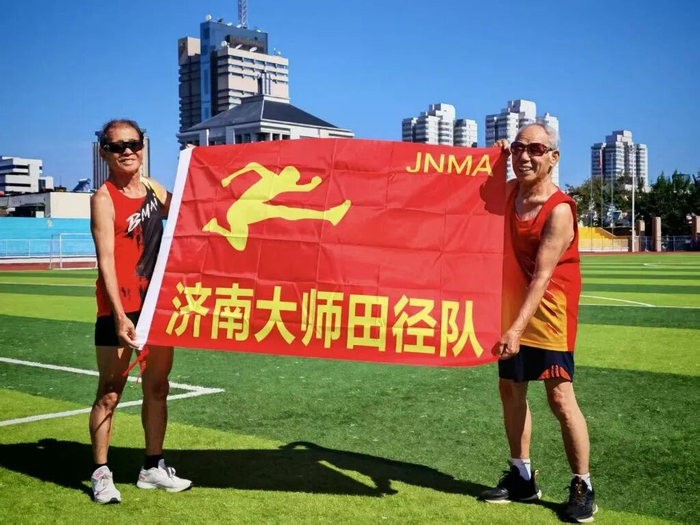 吕明璞（右）和队友一起展示济南大师田径队的队旗。受访者供图