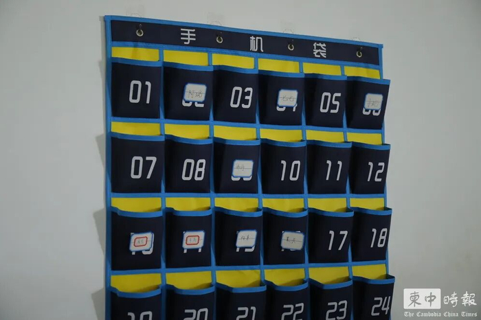 办公区域墙上设置编号“手机袋”，部分位置贴有中文姓名标签。（图：柬中时报）