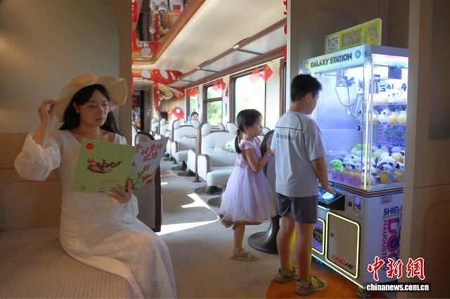 9月27日，江西南昌，一名旅客在“大美上饶”主题观光列车上阅读书籍，旁边的儿童在体验抓娃娃机游戏。中新社记者 刘占昆 摄