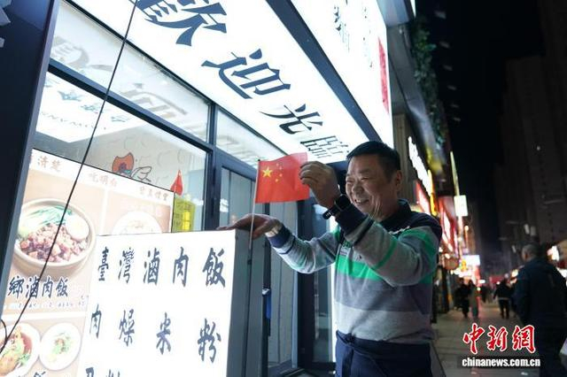 图为10月1日，国庆节，李兴忠在店外的牌匾上挂上国旗。中新社记者 赵宇航 摄 