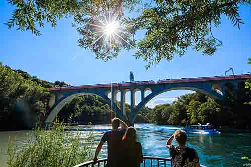 资料图：在瑞士日内瓦，一列火车从架设在罗纳河上的铁路桥上经过。（新华社）