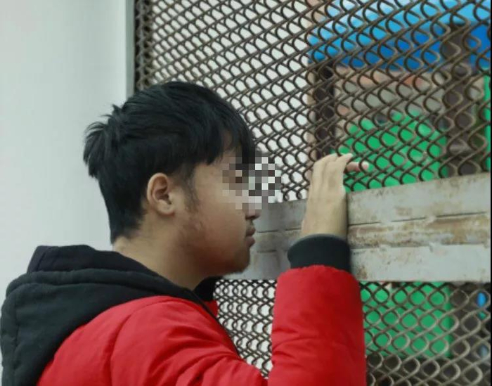 程智斌透过铁锈的栅栏望向学校。9958华西执行团队 摄