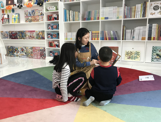 　北京蒲蒲兰绘本馆，两个孩子在老师的指导下阅读绘本。