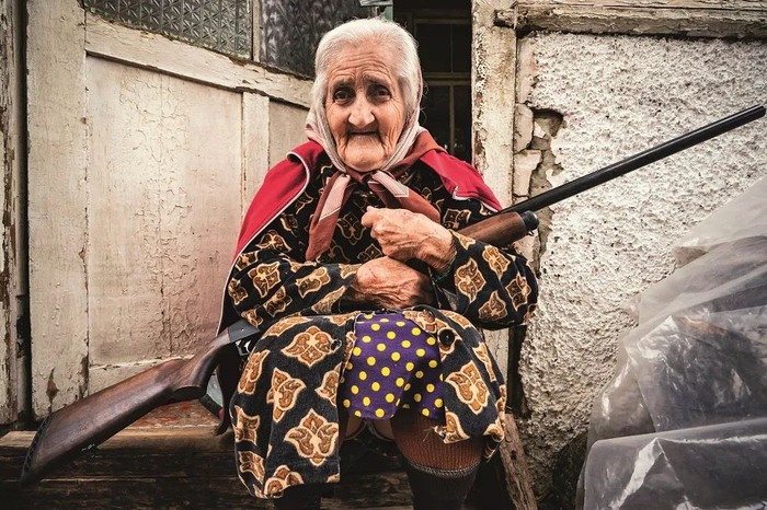  10月4日，纳卡地区首府斯捷潘纳克特，一名老妇人怀抱枪支守在家门口。图/人民视觉&nbsp;