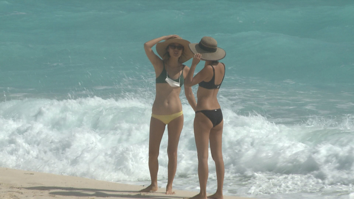 △图为坎昆沙滩上的国际游客 胸前挂着口罩