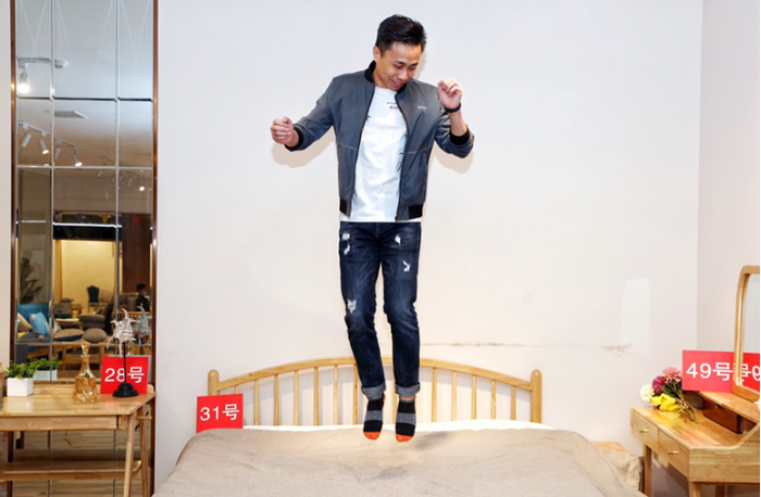 ▲为了证明自己公司的产品质量过硬，毛晶晶在木床上高高地跃起。