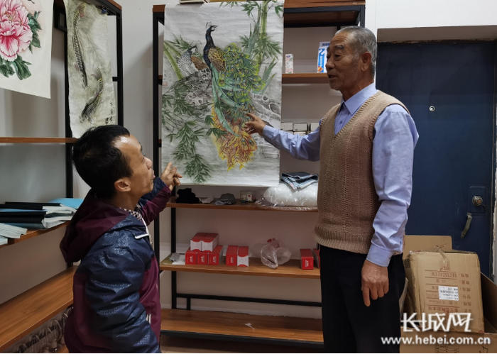 边学强（左）在“爱心扶贫超市”向人们介绍自己的绘画作品。长城网记者 郭庆敏 摄
