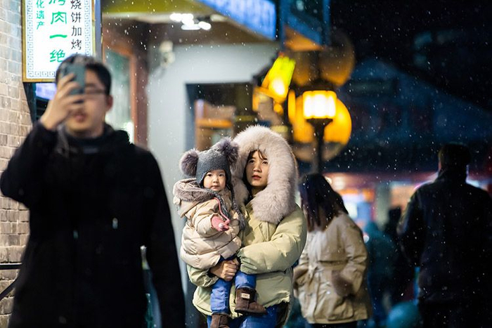烟袋斜街，家长在雪中抱紧孩子。