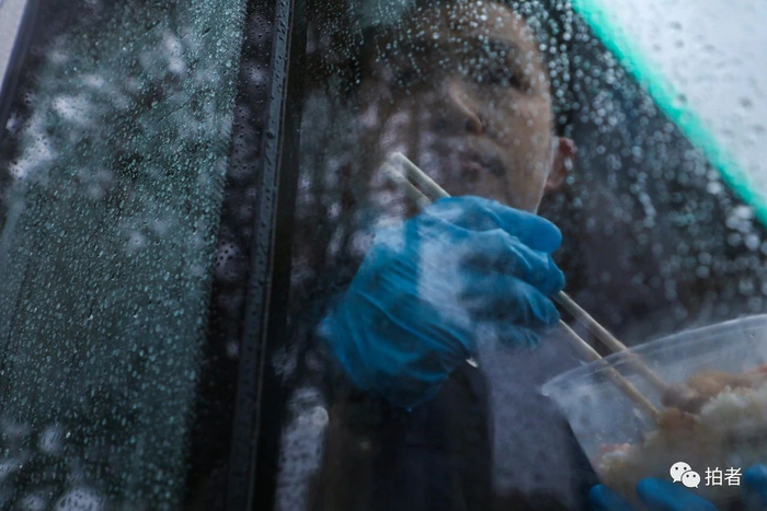  △&nbsp;晚餐时间，雨越来越大，负责值守火神山医院卡点的武汉市公安局蔡甸分局新农派出所民警燕占飞，在警车里边吃饭边观察着卡点周围的情况。摄影/长江日报记者陈卓