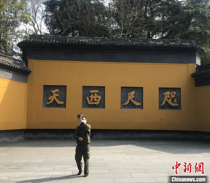     图为杭州灵隐飞来峰景区大门口，一位游客在自拍。　严格　摄