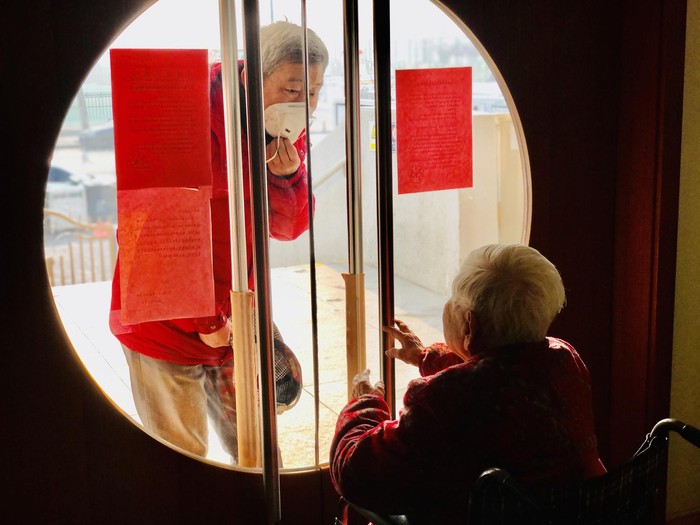 隔离期间，朝阳区双合家园一养老院里，在院老人家属透过楼门玻璃与老伴儿打招呼。受访者供图