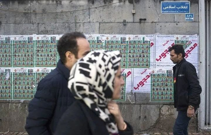 2月20日，在伊朗首都德黑兰，行人走过印有议会选举候选人的海报　图|新华社　摄|艾哈迈德·哈拉比萨斯