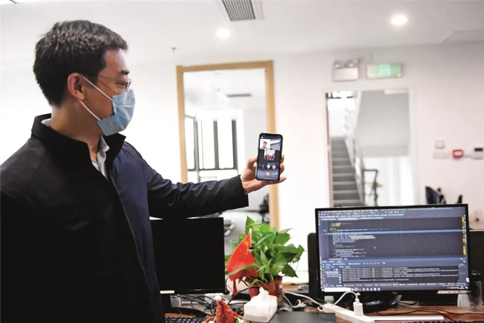 2月11日，位于广州南沙区锦珠广场的中科智城（广州）信息科技有限公司内，空无一人的办工位上几台电脑正在运行，显示器上的代码不时滚动。该企业的技术研发人员正远在家中，通过网络连接远程操作公司电脑，实现在线办公。图为该公司研发部副总监吴鸿与同事在线沟通。摄影/本刊记者 姬东