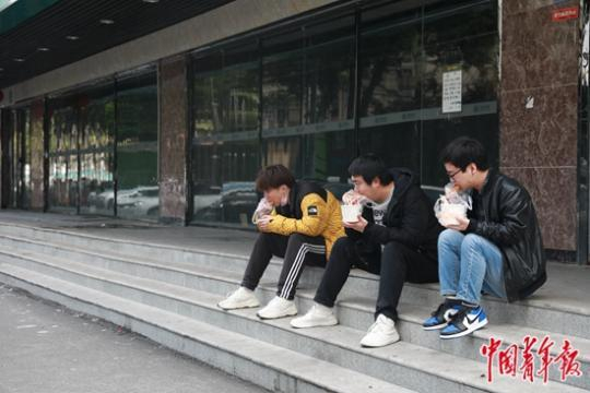  4月3日，武汉铭新街，三位年轻人坐在台阶上吃面窝。中青报·中青网见习记者 鲁冲/摄