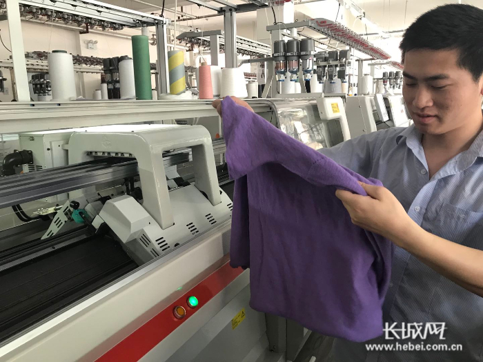 图为慈星一线成型示范工厂车间内，工人展示用一根纱线直接织成的羊绒衫。李萍 供图