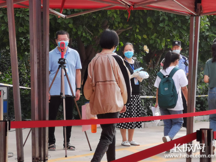 考点工作人员对入场考生进行测温，发放口罩。 魏亚慧 摄