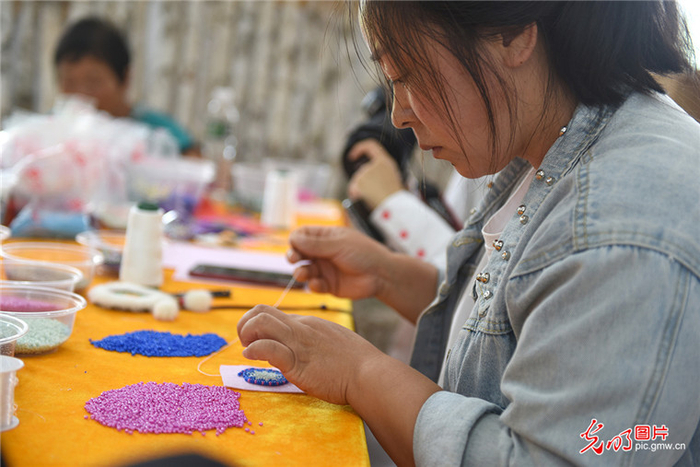 图为8月3日，猎民村的妇女在手工艺中心制作太阳花。（潘迪摄/光明图片）