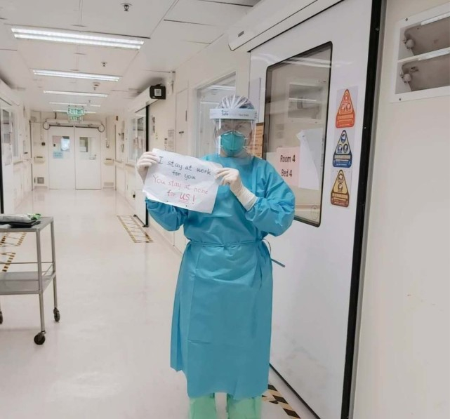 身穿防护服的阿May展示宣传语，呼吁市民减少外出