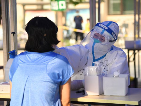 中国制定了严密的措施防控疫情。图为6月23日，在北京市海淀区八里庄街道的一处核酸检测采样点，医护人员（右）为居民进行咽拭子采样。（任超 摄）