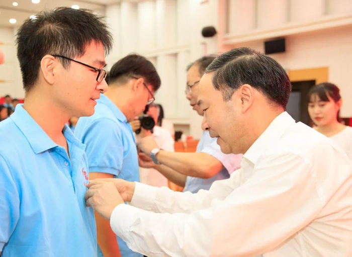 ▲校党委书记姚冠新、校长焦新安为新入职教师代表佩戴校徽。当刻有“扬州大学”字样的校徽佩于胸前，标志着全体新入职教师正式加盟扬州大学大家庭！